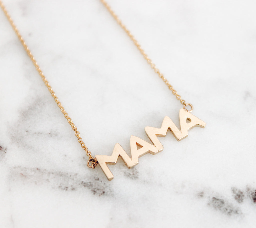 14K Yellow Gold mama necklace on a marble slab.